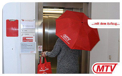 Eine Frau mit rotem MTV-Regenschirm steigt in einen Aufzug: ...mit dem Aufzug...