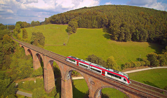 Ein Zug fährt über ein Viadukt, Hintergrund grüne Landschaft