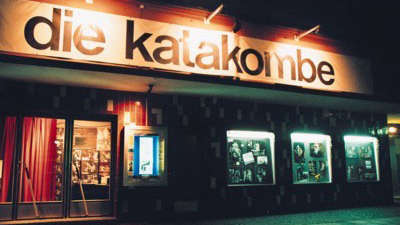 Exterior view of the theater at night with the illuminated sign "Katakombe"
