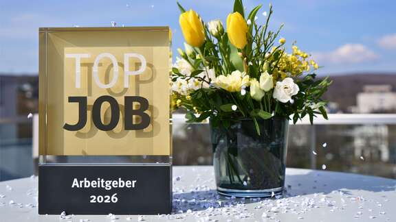 TOP-JOB-2026-Auszeichnung auf einem Tisch mit Frühlingsblumenstrauß.
