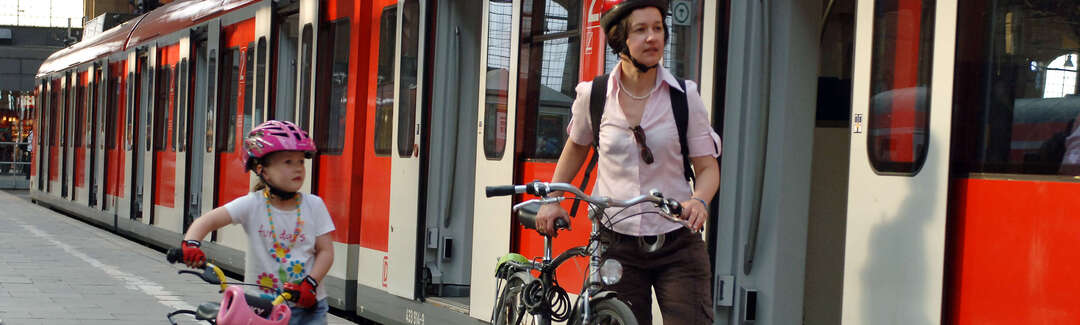 Woman and a young girl with bikes on the platform next to a red train with opened doors