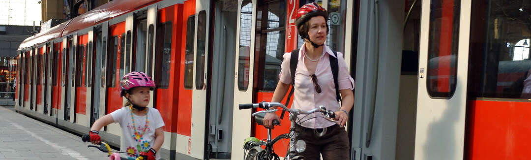Frau und Mädchen schieben ihre Fahrräder am Bahnsteig neben Zug mit geöffneten Türen