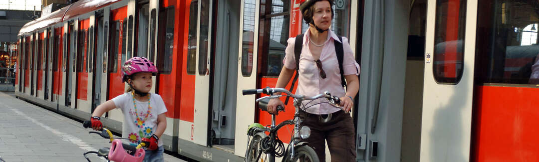 Frau und Mädchen schieben ihre Fahrräder am Bahnsteig neben Zug mit geöffneten Türen