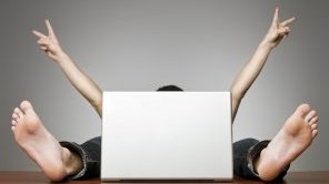 Ein Mann sitzt versteckt hinter einem Laptop. Es sind nur seine Arme und Füße zu sehen