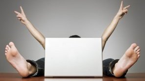 Ein Mann sitzt versteckt hinter einem Laptop. Es sind nur seine Arme und Füße zu sehen