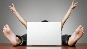 Ein Mann sitzt versteckt hinter einem Laptop. Es sind nur seine Arme und Füße zu sehen