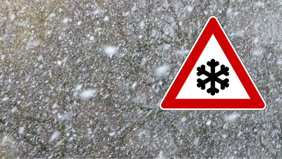 Schneesturm und ein Achtungsschild mit Schneekristall