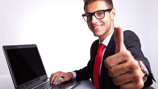 Ein Mann sitzt mit erhobenem Daumen vor einem Laptop