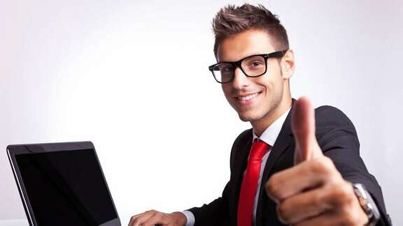 Man with suit and tie sitting in front of a laptop with a thumb up