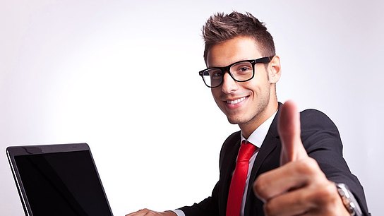 Ein Mann sitzt mit erhobenem Daumen vor einem Laptop