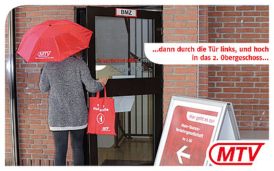 Eine Frau mit rotem MTV-Regenschirm geht durch die Glastür mit der Aufschrift "Gewerbekunden Center Obergeschoß": ...dann durch die Tür links, und hoch in das 2. Obergeschoss...
