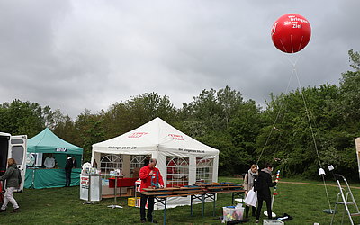 Ein Mann baut Tische auf. Der MTV-Pavillon sowie ein MTV-Ballon mit de Aufschrift "Wir bringen Sie ans Ziel" befinden sich im Hintergrund.