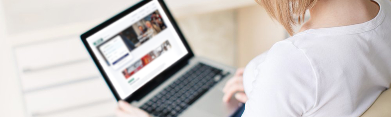 Eine Frau sitzt mit einem Laptop auf dem Schoß in einem beigen Sessel. Man sieht die Webseite RMV aktuell