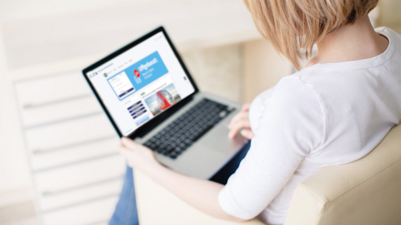 Eine Frau sitzt mit einem Laptop auf dem Schoß in einem beigen Sessel. Man sieht die Webseite RMV aktuell