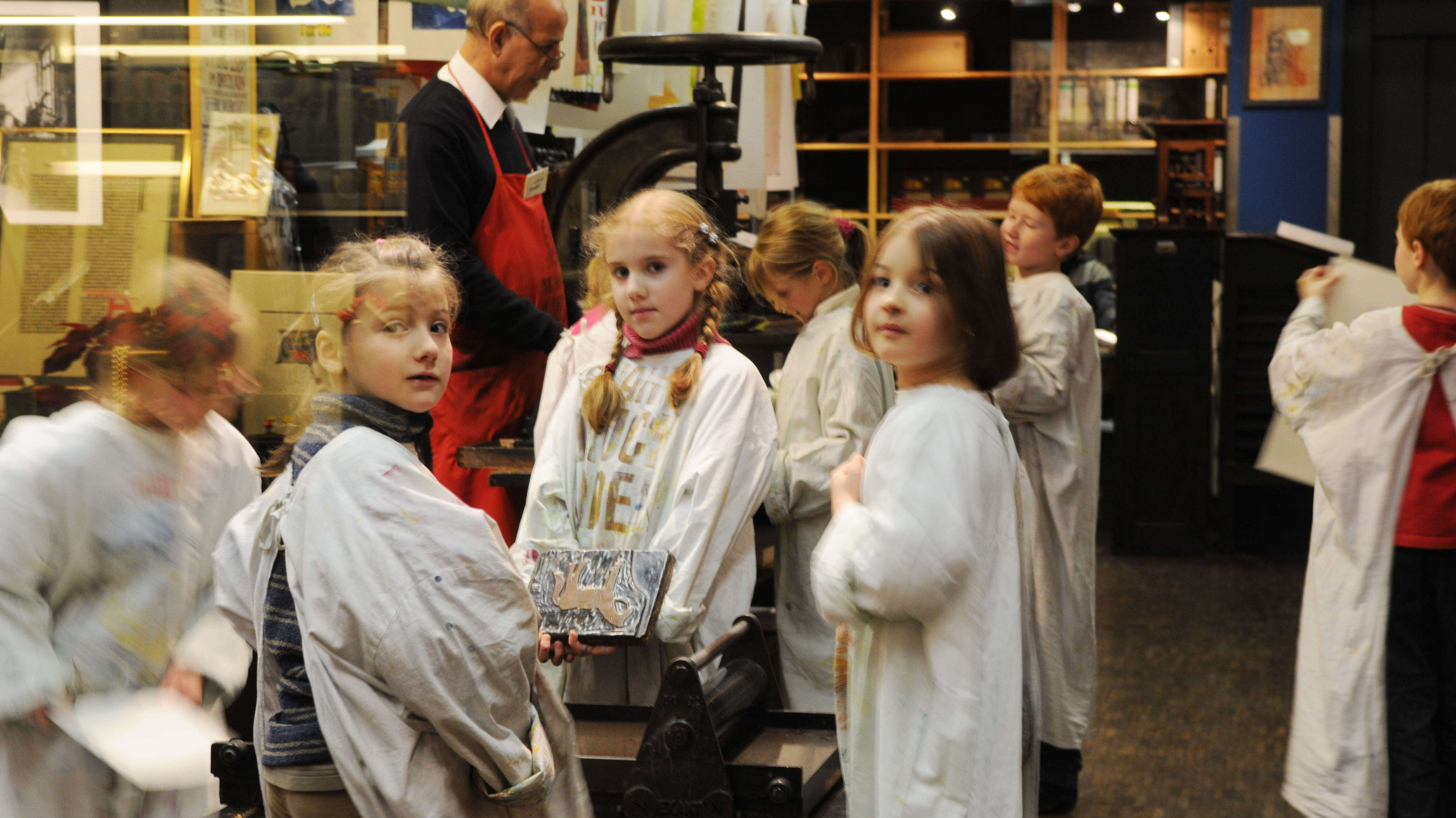 Kinder im Druckladen des Gutenbergmuseum in Mainz Kinder in weißen Kitteln drucken an einer Maschine im Druckladen in Mainz