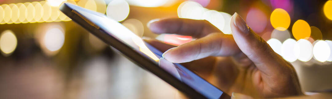 Hände die ein Smartphone bedienen draußen bei Nacht