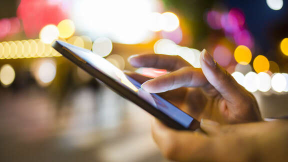 Night scene in the city, hand with mobile phone, fingers typing on display