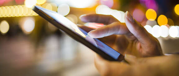 Hände die ein Smartphone bedienen draußen bei Nacht