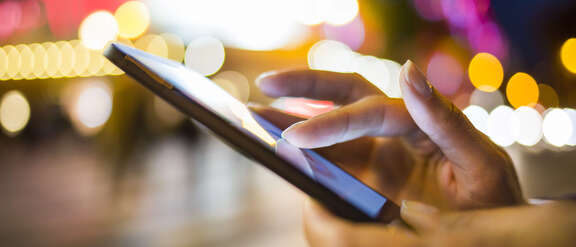 Vergrößerte Ansicht: Hände die ein Smartphone bedienen draußen bei Nacht