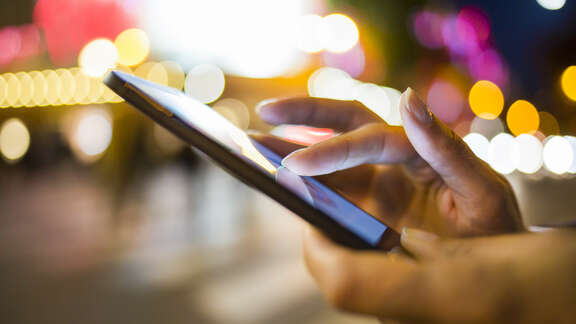 Night scene in the city, hand with mobile phone, fingers typing on display