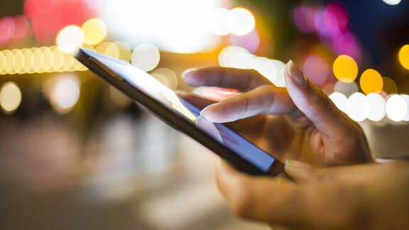 Hände die ein Smartphone bedienen draußen bei Nacht