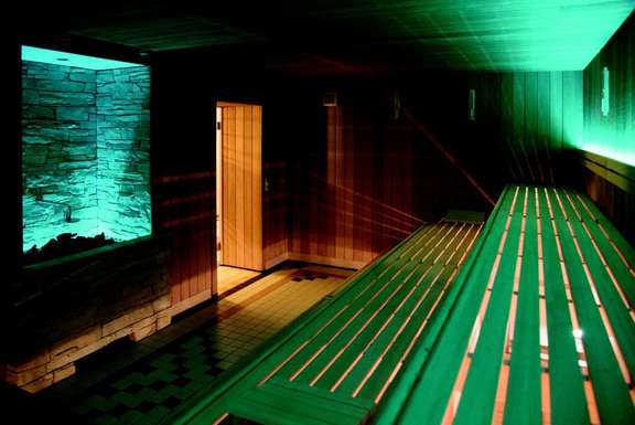 Vergrößerte Ansicht: Innenansicht Sauna mit Holzliegen, Saunaofen, gedämpftes Licht