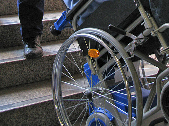 Rollstuhl wird mit Hilfe eines Treppensteigers eine Treppe hinunter bewegt