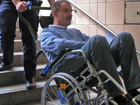 Rollstuhlfahrer wird mit Hilfe eines Treppensteigers eine Treppe hinunter bewegt