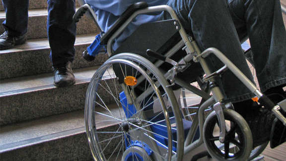 Rollstuhlfahrer wird mit Hilfe eines Treppensteigers eine Treppe hinunter bewegt
