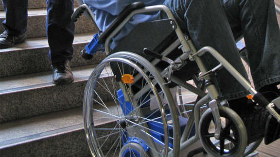 An employee helps a man in a wheel chair down the steps