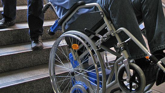 Rollstuhl wird mit Hilfe eines Treppensteigers eine Treppe hinunter bewegt