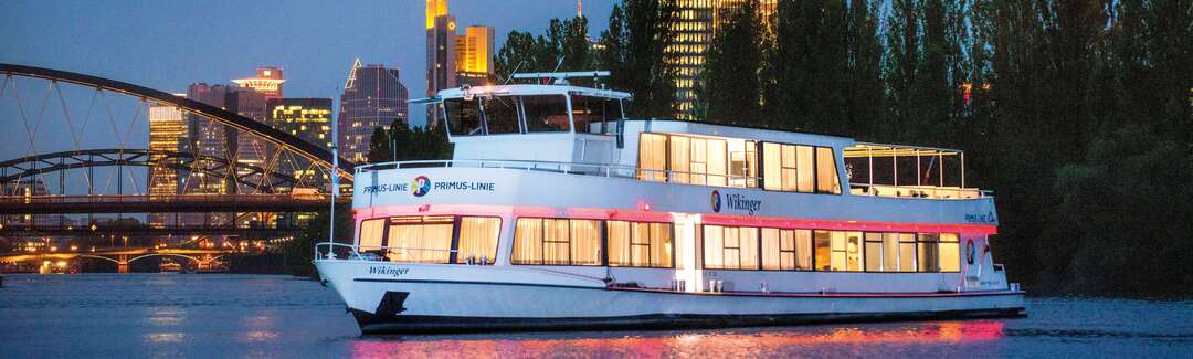 Ausflugsschiff vor der beleuchteten Frankfurter Syline am Abend