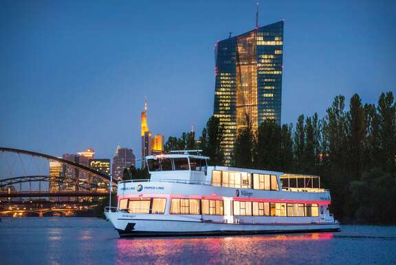 Ausflugsschiff vor der beleuchteten Frankfurter Syline am Abend