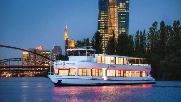 Ausflugsschiff vor der beleuchteten Frankfurter Syline am Abend