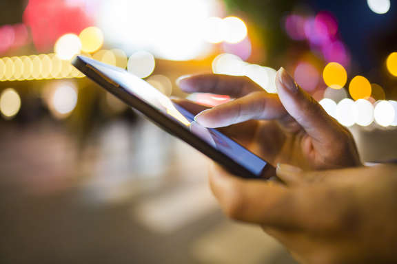 Night scene in the city, hand with mobile phone, fingers typing on display