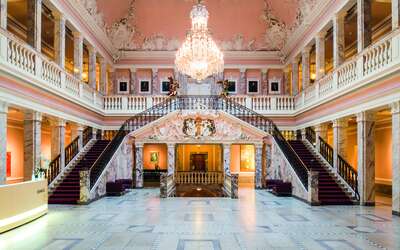 Der Marmorsaal mit Kronleuchter, doppeltem Treppenaufgang und Empore mit Säulengängen.