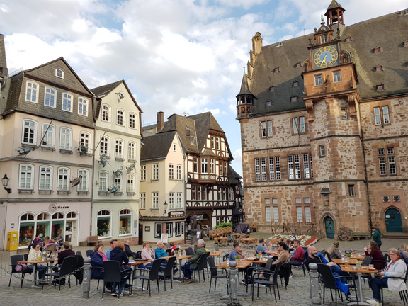 Marburg mehrere Menschen an Tischen sitzend auf gepflastertem Platz vor historischem Steinhaus