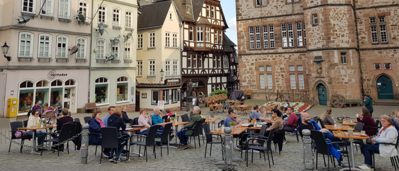 Marburg mehrere Menschen an Tischen sitzend auf gepflastertem Platz vor historischem Steinhaus