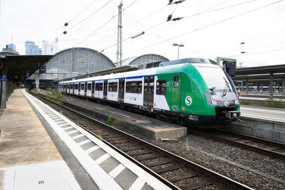 weiße S-Bahn mit grünem Triebwagen auf einem offenen Gleis im Bahnhof. 