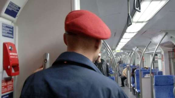 Man with red cap and blue uniform seen from behind in a suburban train