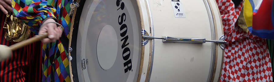 verkleidete Person trägt eine große Trommel