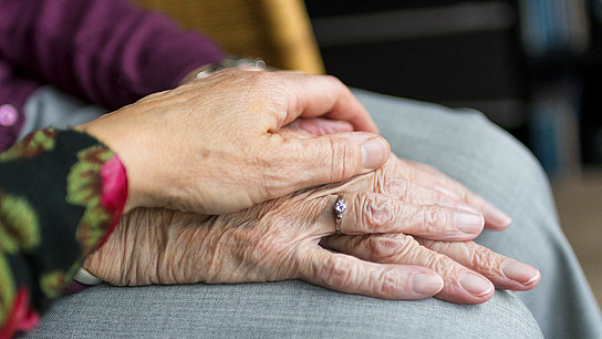 Eine junge Hand liegt fürsorglich auf alten Händen.