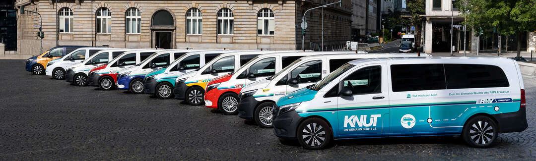 Verschiedene Fahrzeuge stehen in einer Reihe versetzt vor einem Gebäude. Seitliche Sicht auf die Fahrzeugflotte