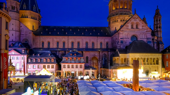 Blick von oben auf den Markt, der mit Menschen gefüllt ist, die unter weißen Schirmen sitzen. Links steht eine Bühne, im Hintergrund ist der Dom.