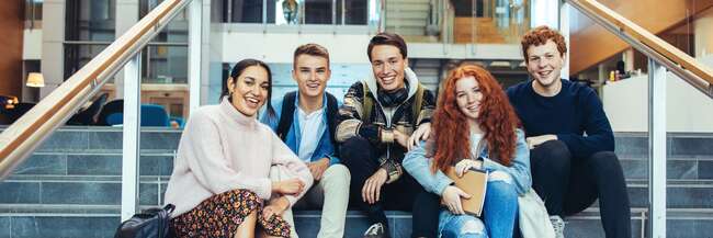 Fünf Schülerinnen und Schüler sitzen in einem Gebäude auf Treppenstufen