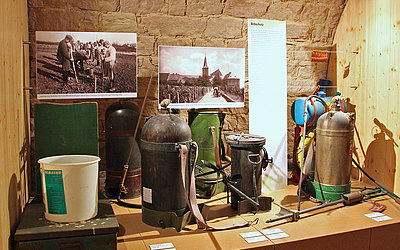 Vergrößerte Ansicht: alte Kanister und zwei alte Fotos in Museumsausstellung