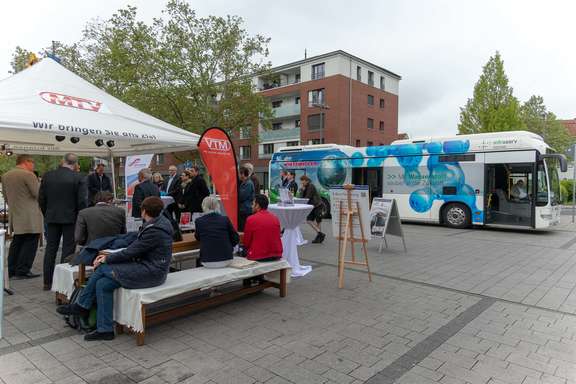 Eine Gruppe Menschen hört Herrn Baron bei einem Vortrag zu. Ein Elektrobus befindet sich im Hintergrund. Roadshow zur Elektromobilität im ÖPNV am 17.05.