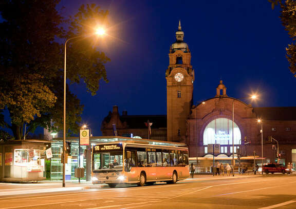 Bus in the dark stopping at a bus stop in front of a station building