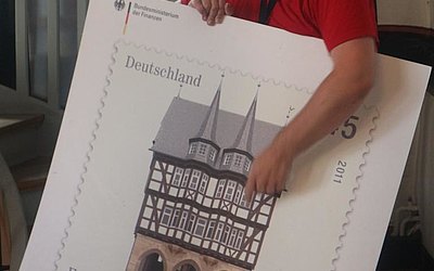 Vergrößerte Ansicht: Mann hält Briefmarke in groß mit Fachwerkhaus