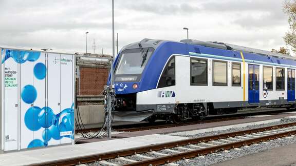 Coradia iLint Blau-weißer Nahverkehrszug neben Wasserstofftankstelle